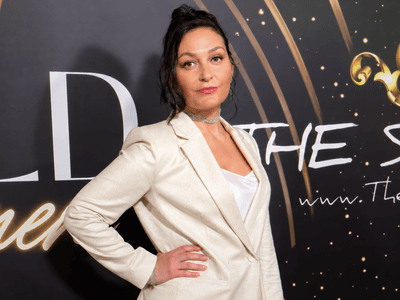 Woman in a blazer poses confidently at a glamorous event backdrop