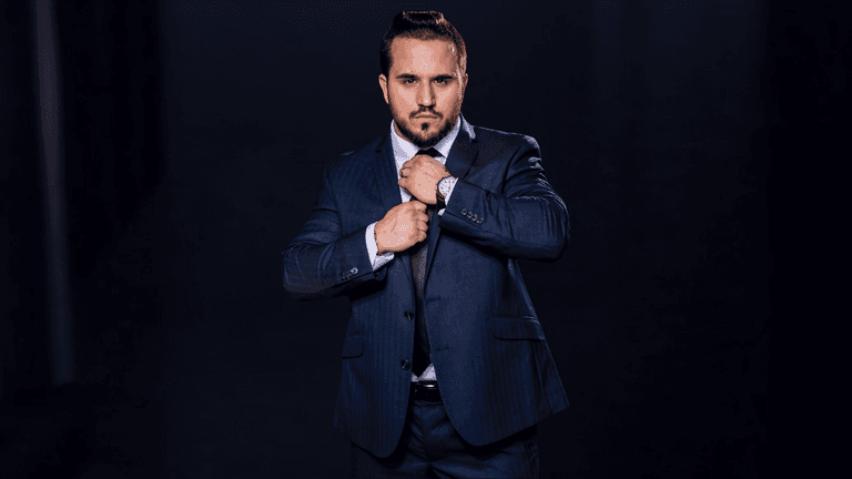 Man in a blue suit adjusting his tie against a dark background