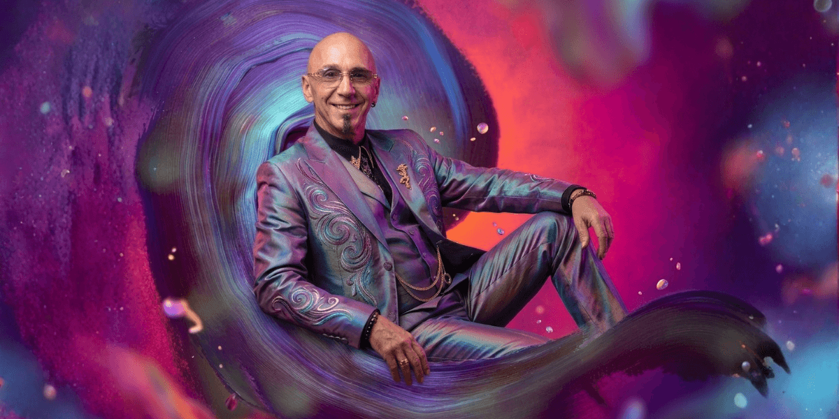A man in a colorful suit sits against a vibrant, swirling background