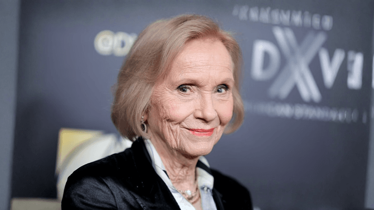 Elderly woman with short blonde hair smiling at an event backdrop